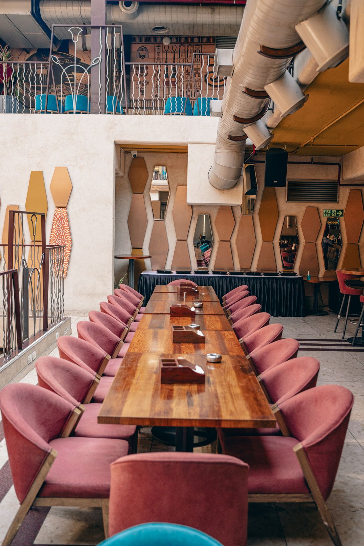 Long communal table with rose-pink chairs under hieroglyph walls