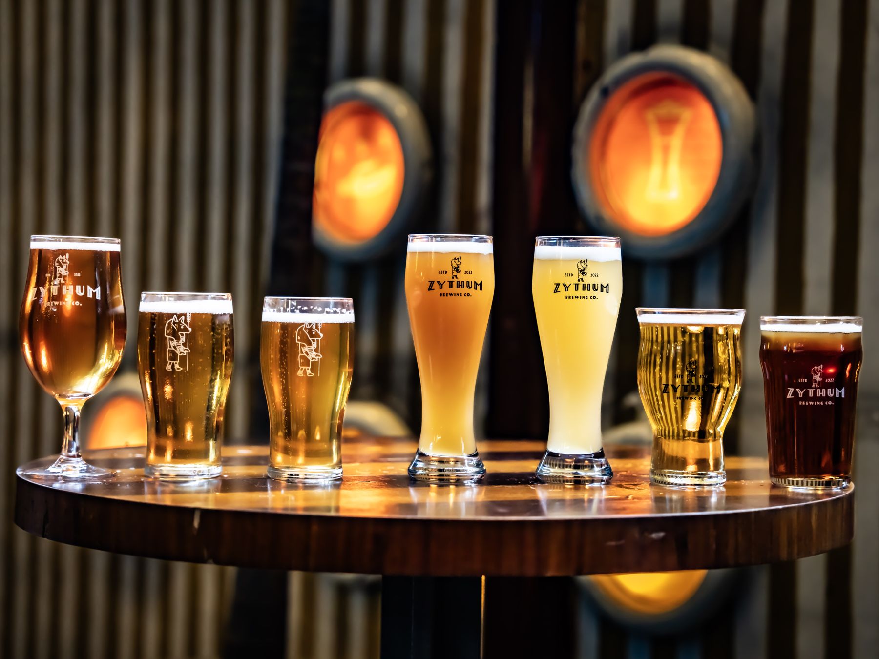Zythum's house beers lined up on a barrel table under warm lamplight